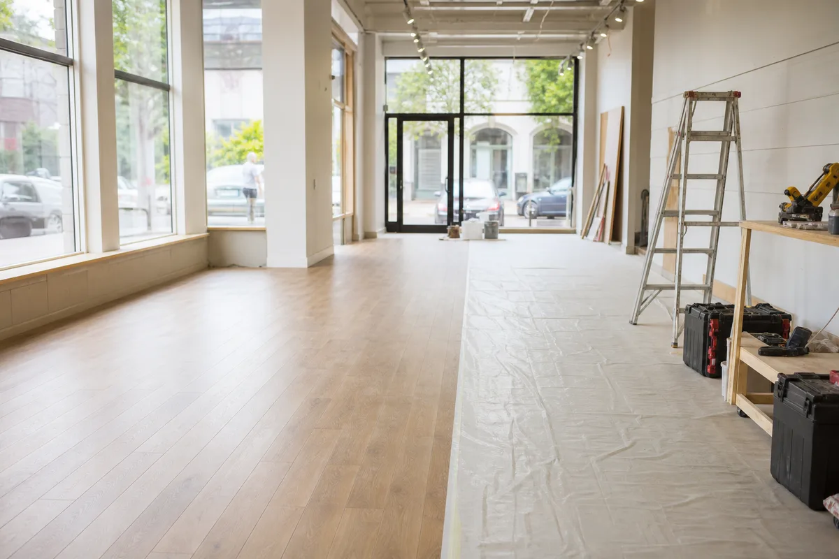 Intérieur de commerce en travaux de rénovation, sol neuf en cours de pose et matériel d’artisan aligné le long du mur