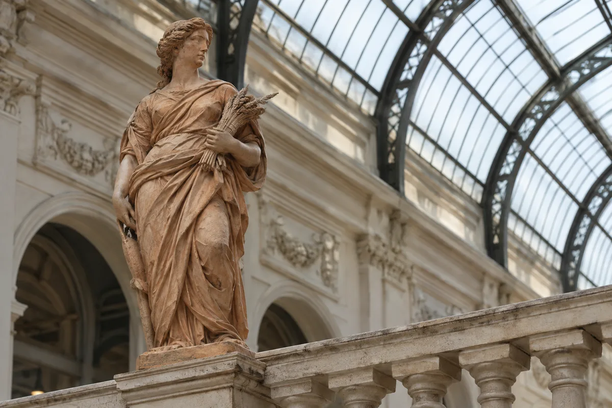 Statue allégorique en terre cuite sur une balustrade de galerie couverte éclairée par la lumière du jour