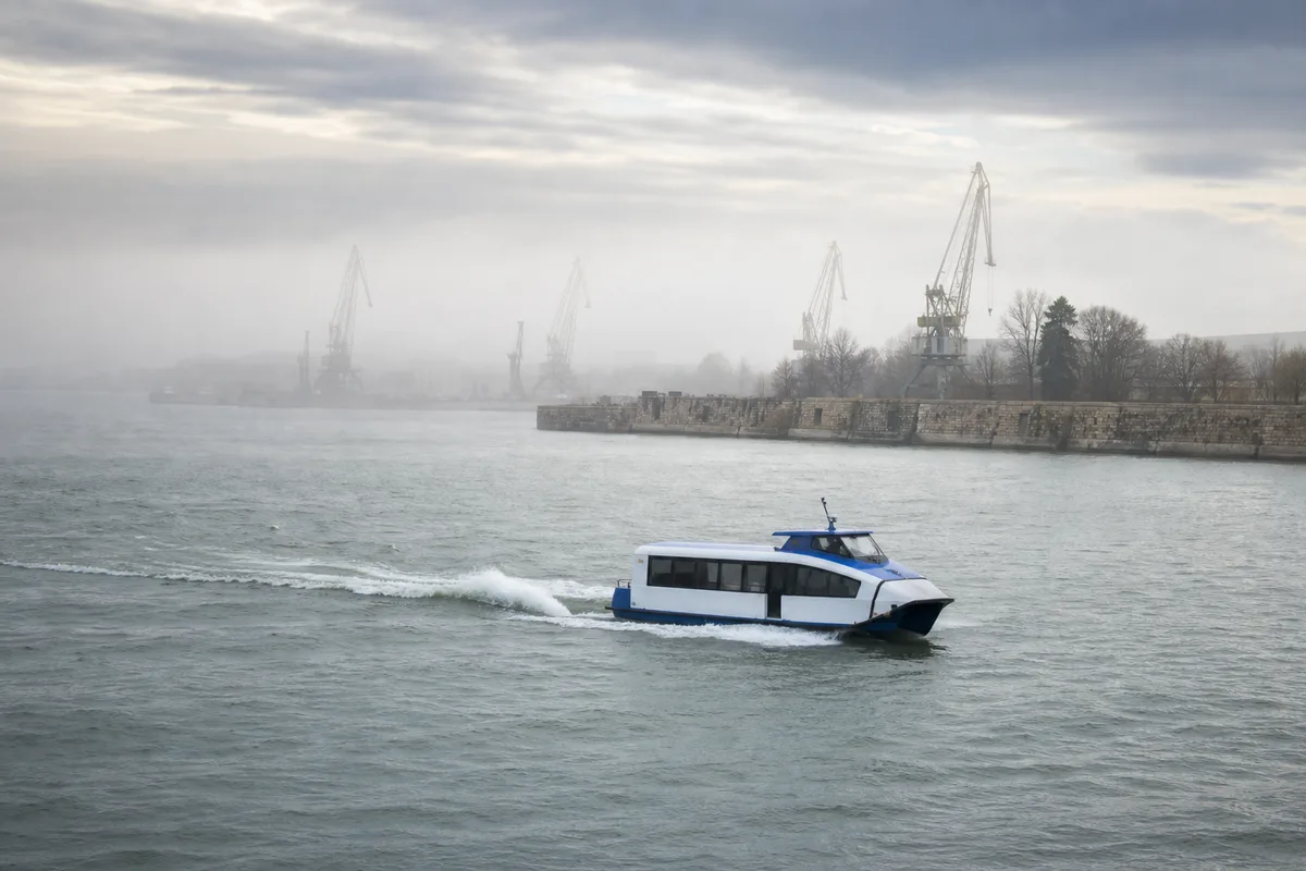 Bateau navette fluvial traversant un large fleuve sous un ciel gris
